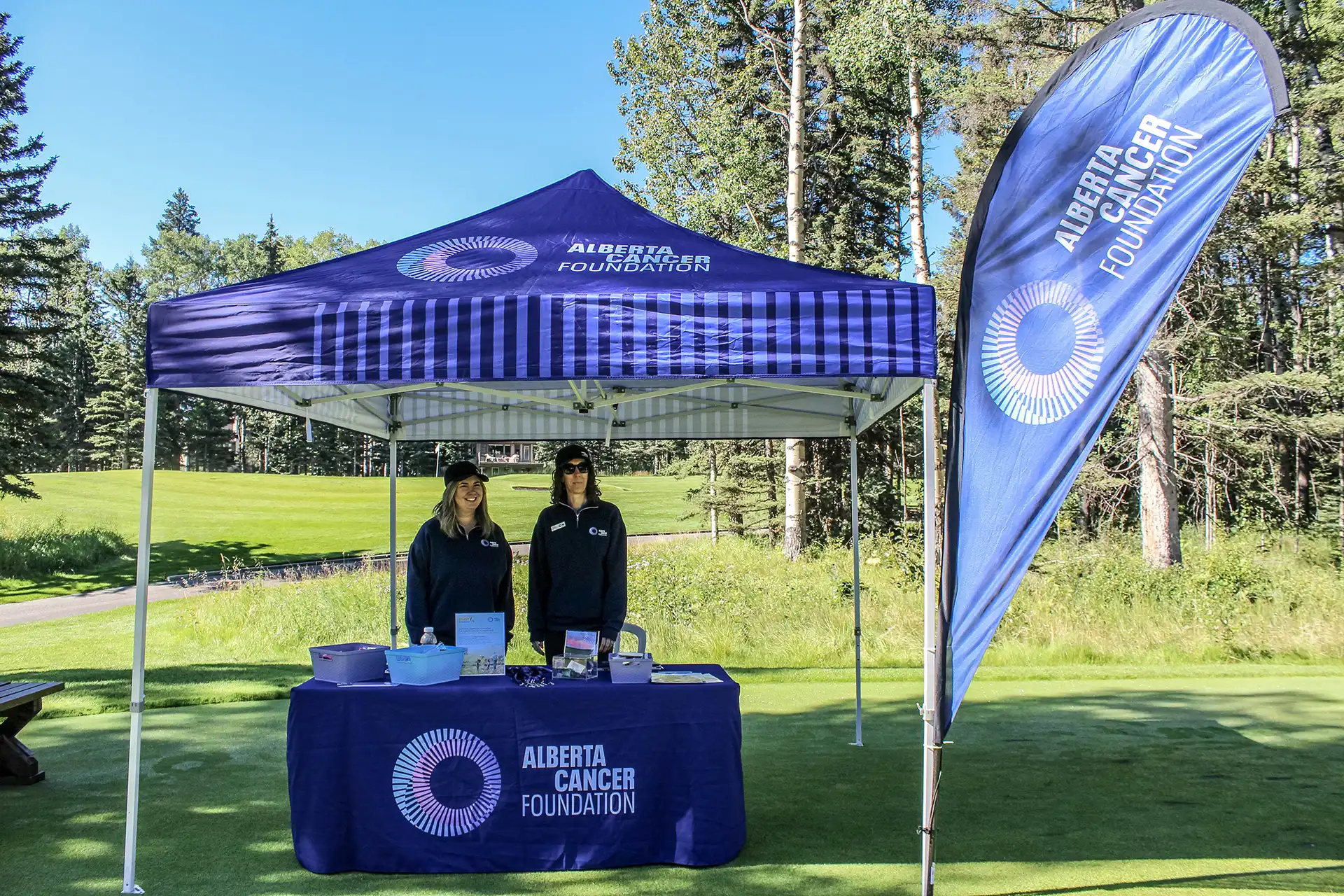 Blue Prostate Cancer Centre tent and banner with volunteers running a 50/50 raffle on the golf course at Priddis Greens during the AGAT Priddis Greens Charity Classic.